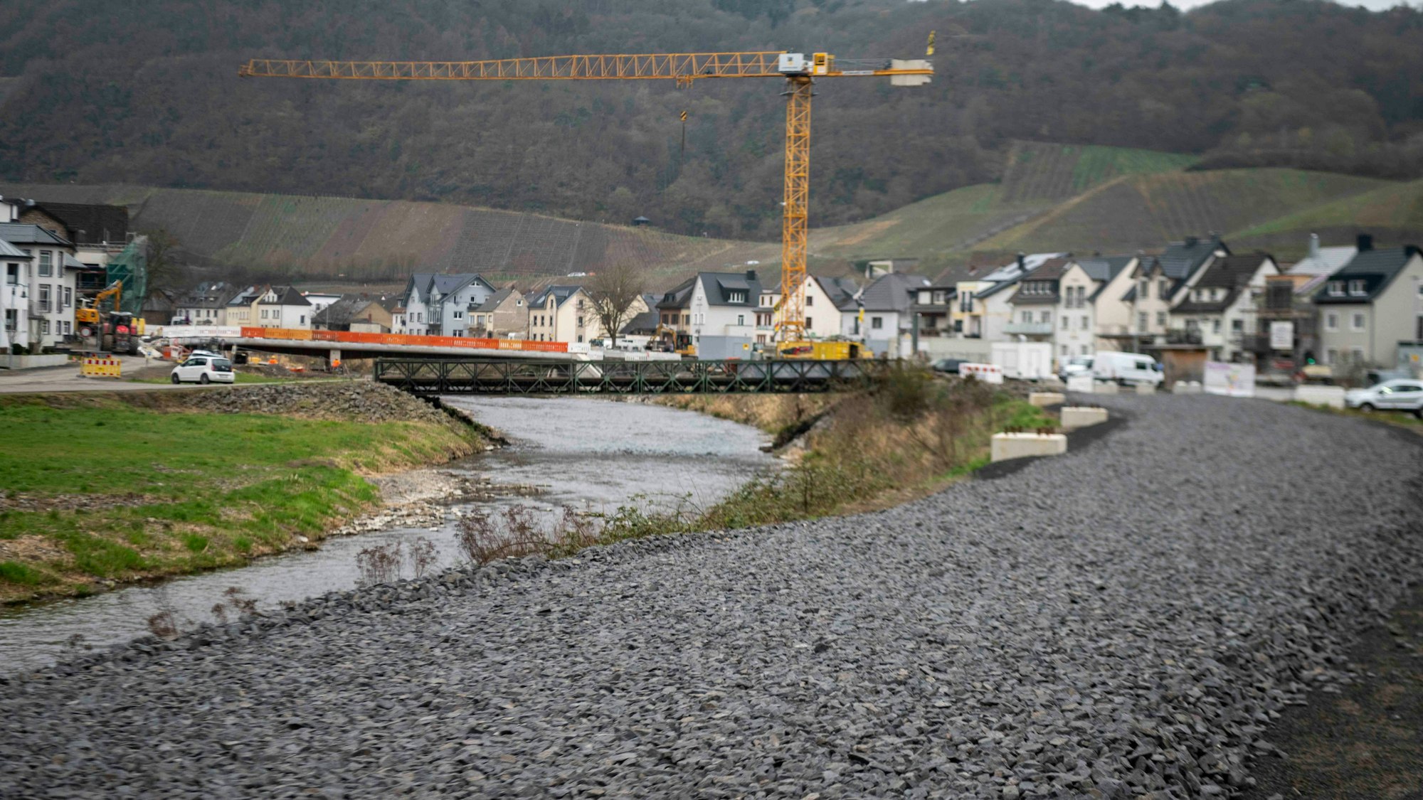 Am Rand der Ahr ist das Gleisbett zu sehen, im Hintergrund der Ort Dernau mit einem alles überragenden Kran.