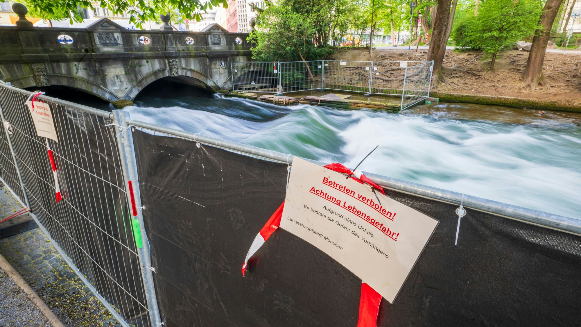 Eine umfangreiche Absperrung verhindert aktuell das Surfen auf der künstlichen Welle am Eisbach im Englischen Garten in München.
