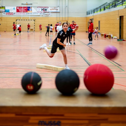 Ein Mädchen versucht, mit einem Ball andere Bälle zu treffen.
