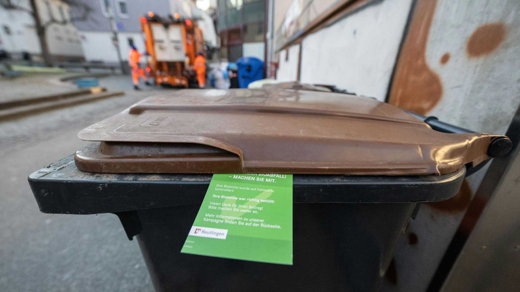 Ein grüner Zettel hängt an einer Biomülltonne.