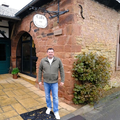 Markus Mathieu steht vor dem Café Zehntscheune in Eicks, das sich in einem historischen Gebäude aus dem Jahr 1613 befindet.