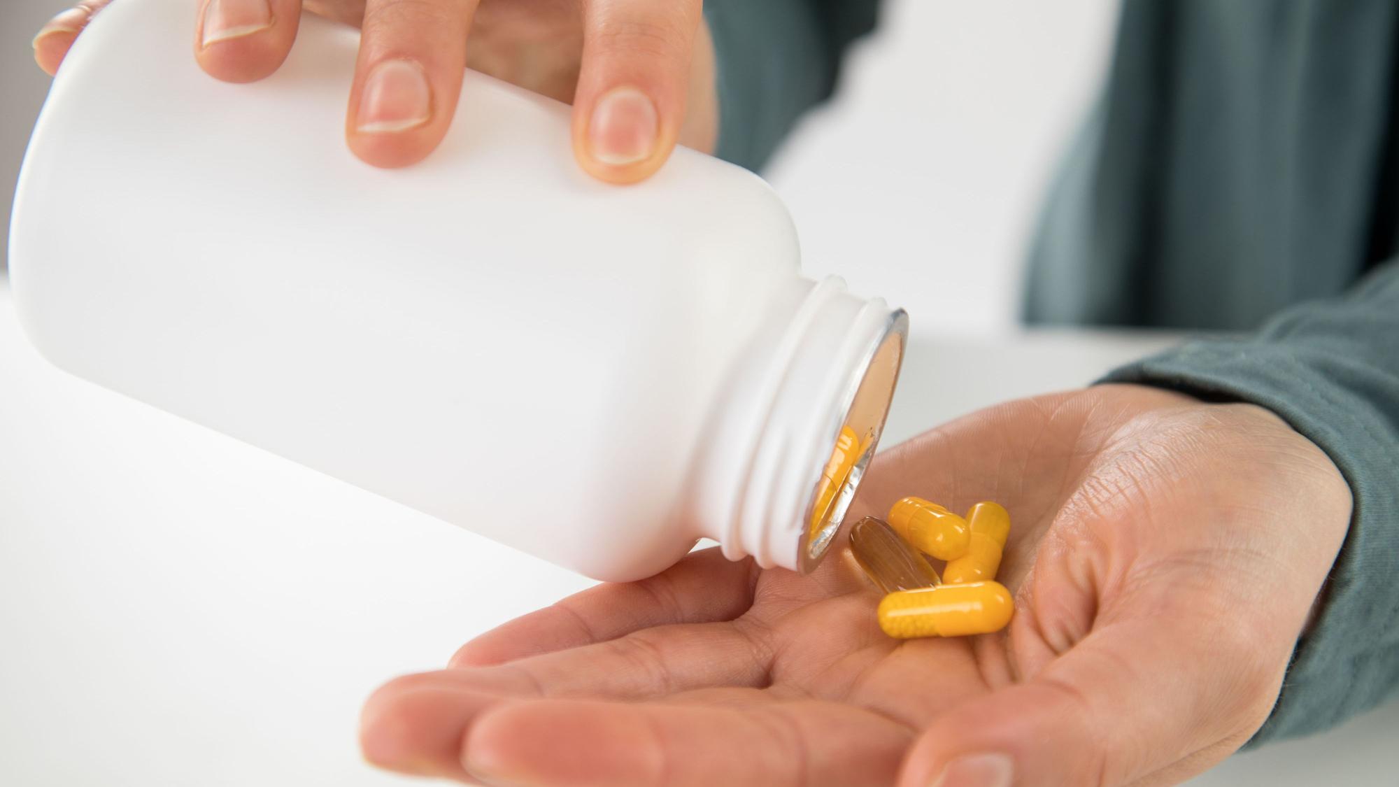 Eine Person schüttet Tabletten aus einer Dose in ihre Hand.