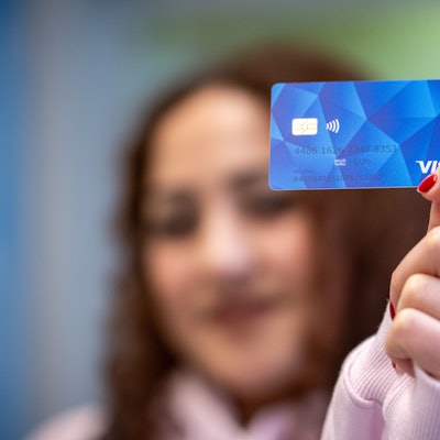 Eine Frau zeigt eine Musterkarte einer sogenannten Bezahlkarte für Geflüchtete.