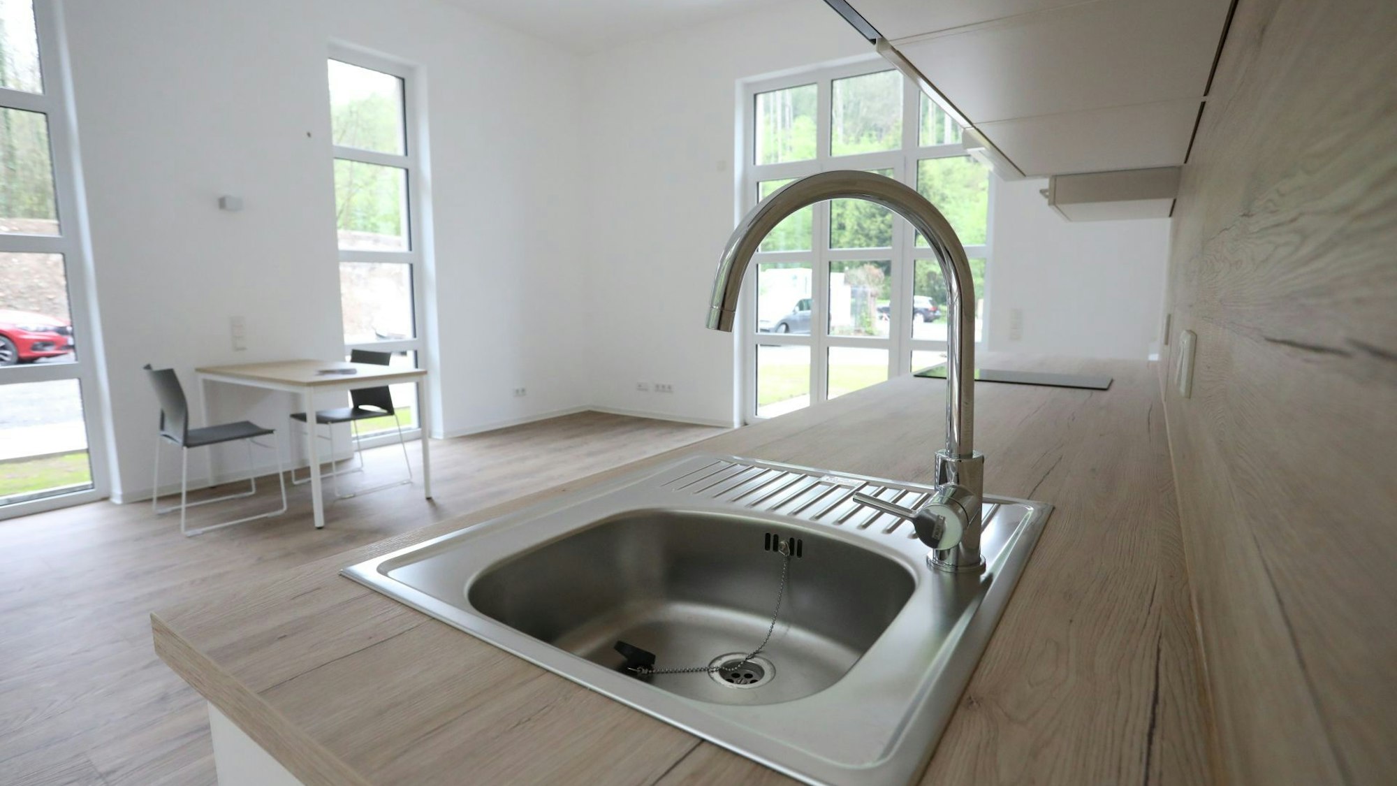 Eine Wohnung, im Vordergrund die Spüle einer Küche, im Hintergrund ein kleiner Tisch mit zwei Stühlen.