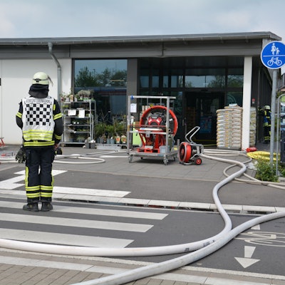 Einsatzkräfte der Feuerwehr mit Schläuchen und einem Großlüfter vor dem Eingang der Aldi-Filiale.