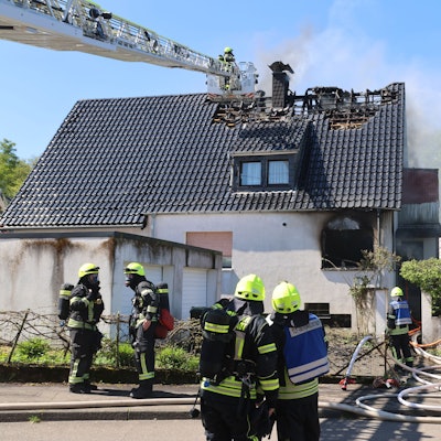 Mehrere Feuerwehrleute löschen, auch per Drehleiter, einen Wohnhausbrand.