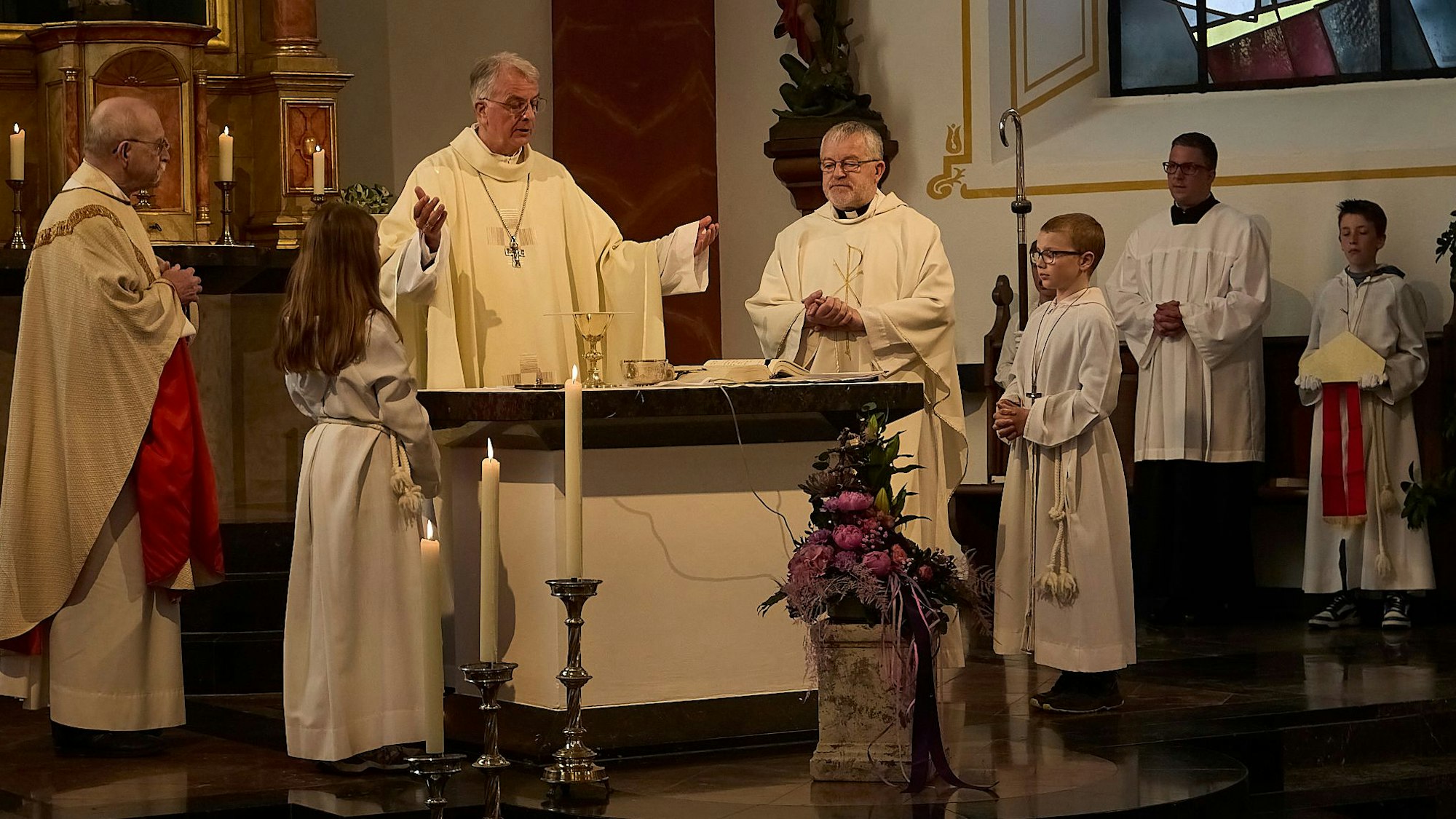 Der Trierer Weihbischof Jörg Michael Peters steht mit ausgebreiteten Armen am Alter in der Kirche in Nettersheim-Tondorf. Neben ihm stehen zwei weitere Priester und vier Messdiener.