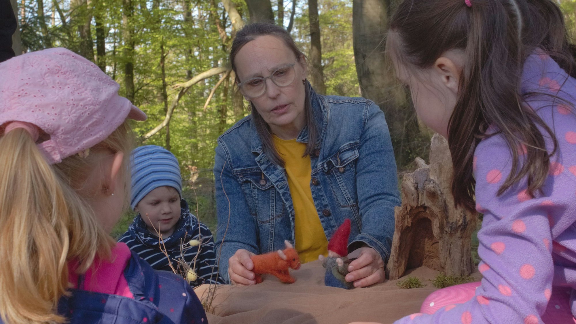 Mithilfe von kleinen Puppen erzählt eine Wanderführerin Kindern im Wald Märchen.