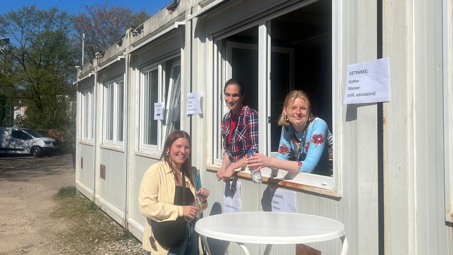 Sie sind an jedem Werktag vor Ort: Sozialarbeiterin Sarah Pollert, die stellvertretende Leiterin Barbara Senzig und Ida Beil, eine studentische Aushilfe. Zwei der Frauen schauen aus einem Fenster des Containers, eine steht davor.
