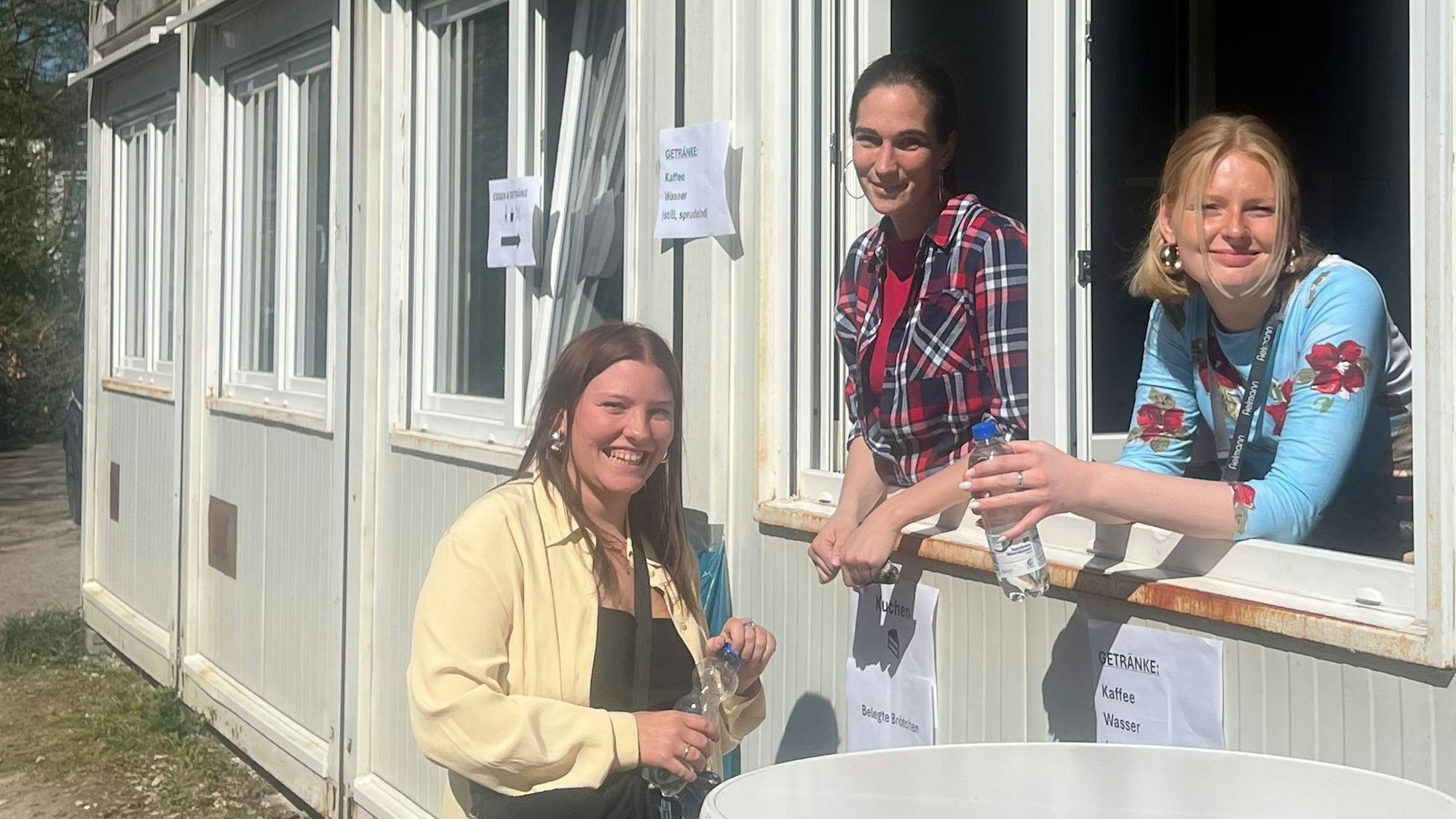Sie sind an jedem Werktag vor Ort: Sozialarbeiterin Sarah Pollert, die stellvertretende Leiterin Barbara Senzig und Ida Beil, eine studentische Aushilfe. Zwei der Frauen schauen aus einem Fenster des Containers, eine steht davor.
