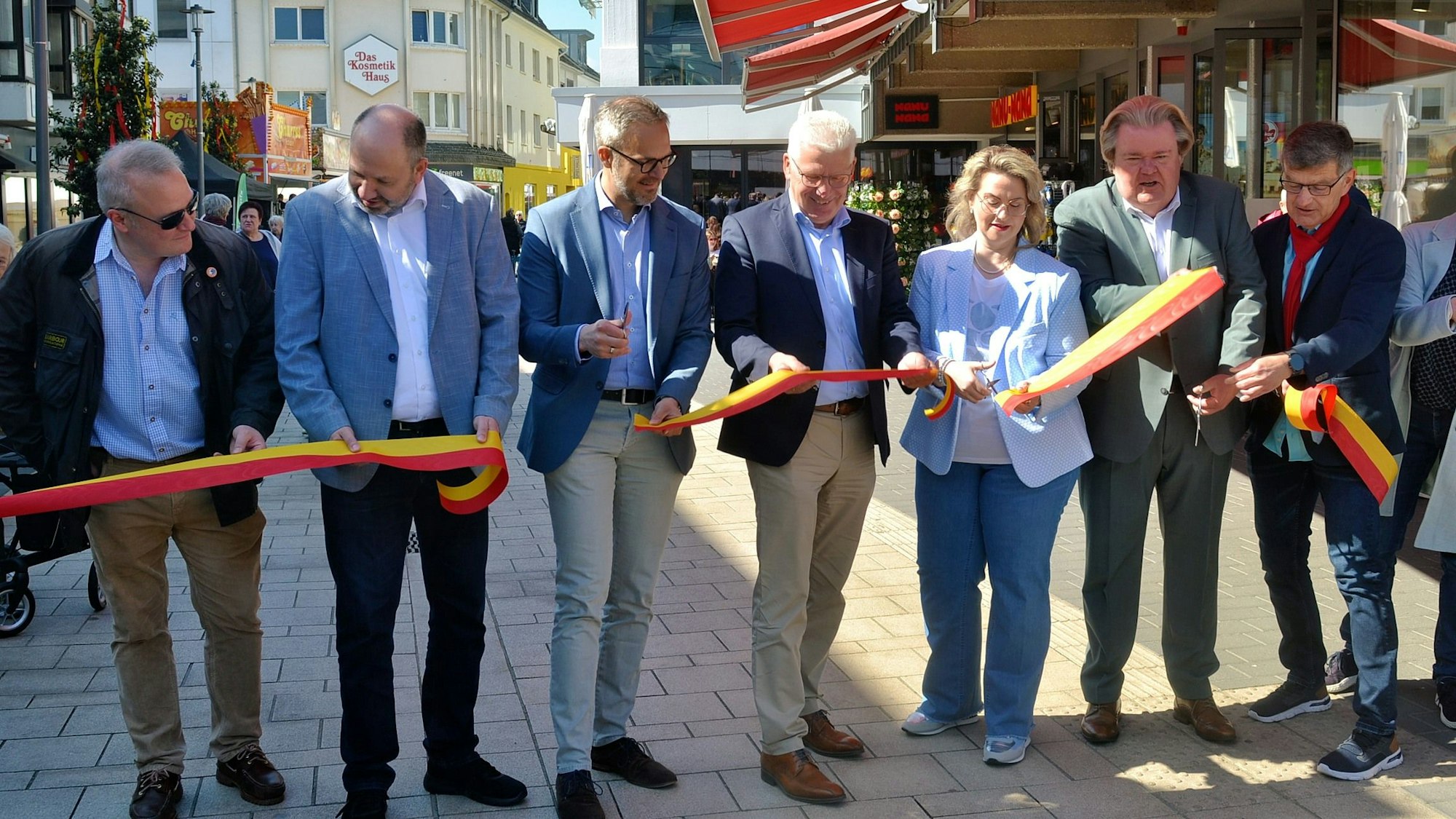 Zur offiziellen Wiedereröffnung der Fußgängerzone in Euskirchen schneiden eine Frau und sechs Männer ein gelb-rotes Band durch.
