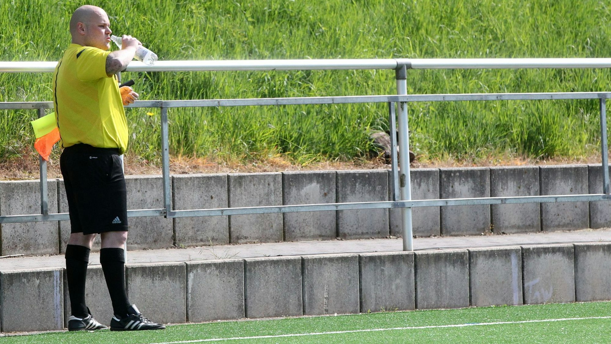 Ein Schiedsrichter-Assistent trinkt am Spielfeldrand aus einer Wasserflasche. Die Fahne hat er sich unter den Arm geklemmt.