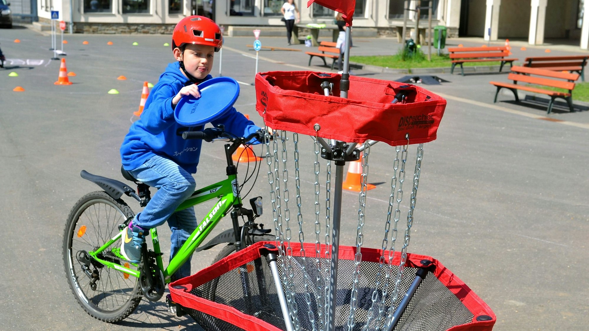 Ein Junge fährt auf dem Fahrrad und zielt mit deinem Frisbee auf einen Korb.