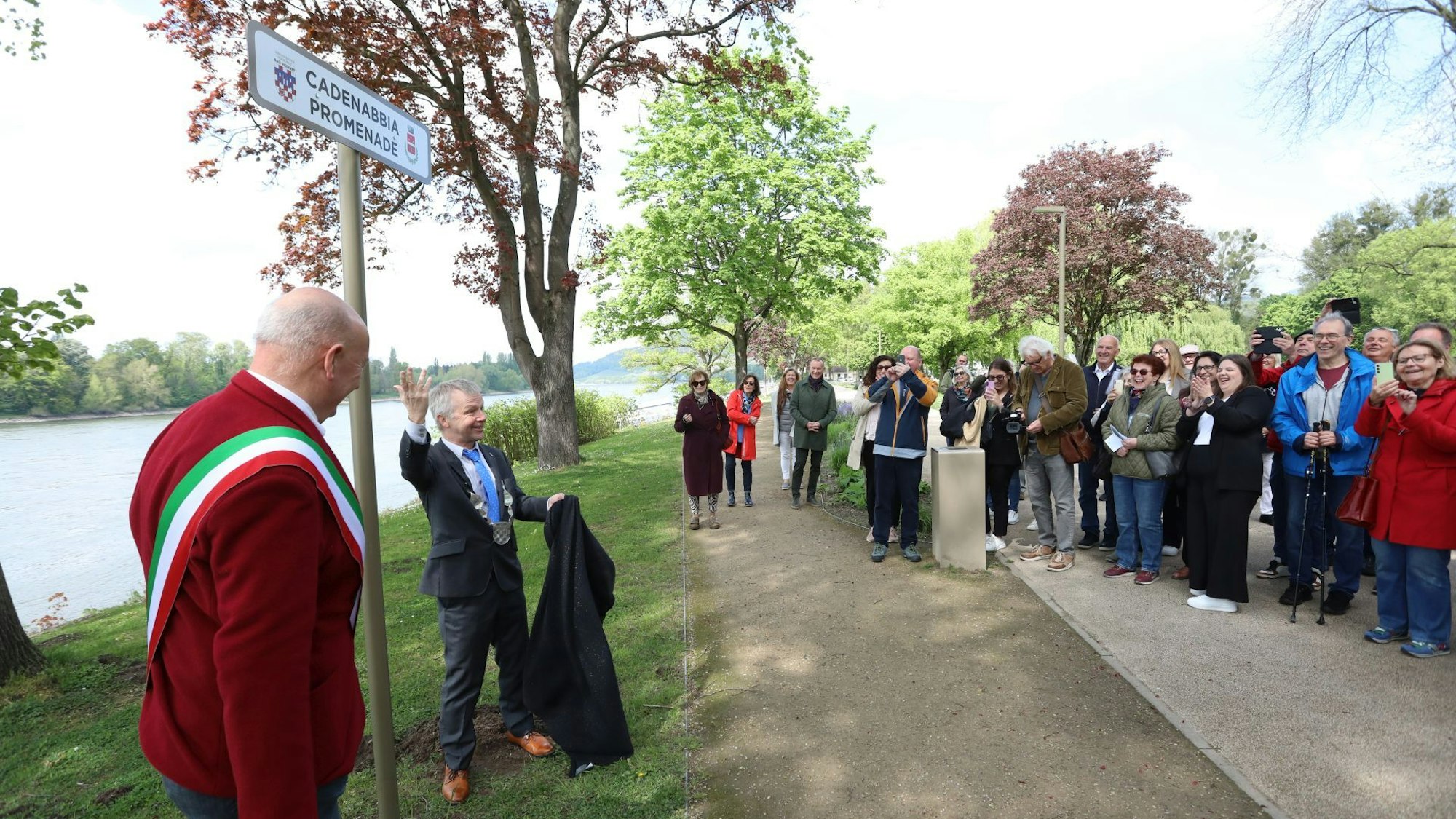 Zwei Männer vor einem Schild "Cadenabbia-Promenade", viele Menschen schauen der Enthüllung zu.