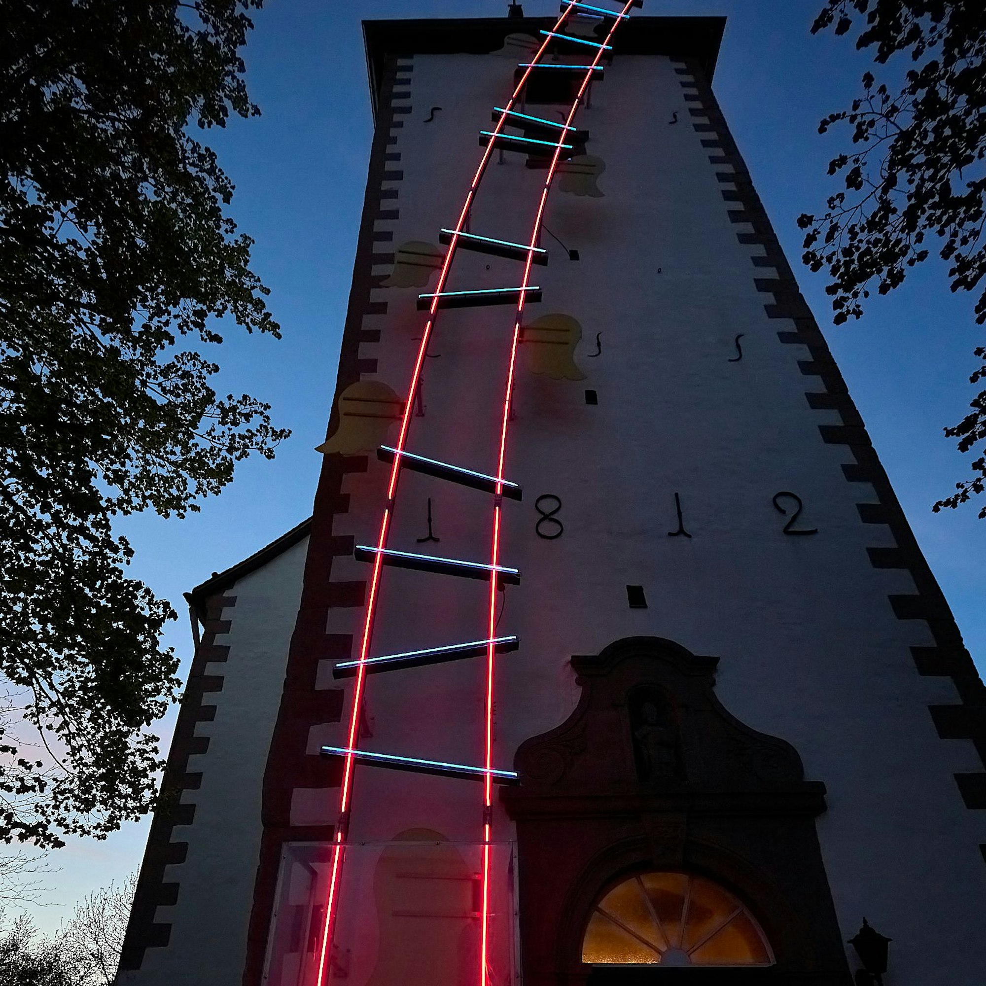 Am Turm der Kirche in Tondorf ist ein 23 Meter hohes Kunstwerk angebracht. In der Nacht ist die Leiter in Rot und Blau bleuchtet.