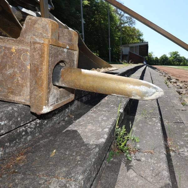 Der überdimensionale Meißel eines Baggers liegt auf Sitzstufen aus Beton, die stark beschädigt sind.