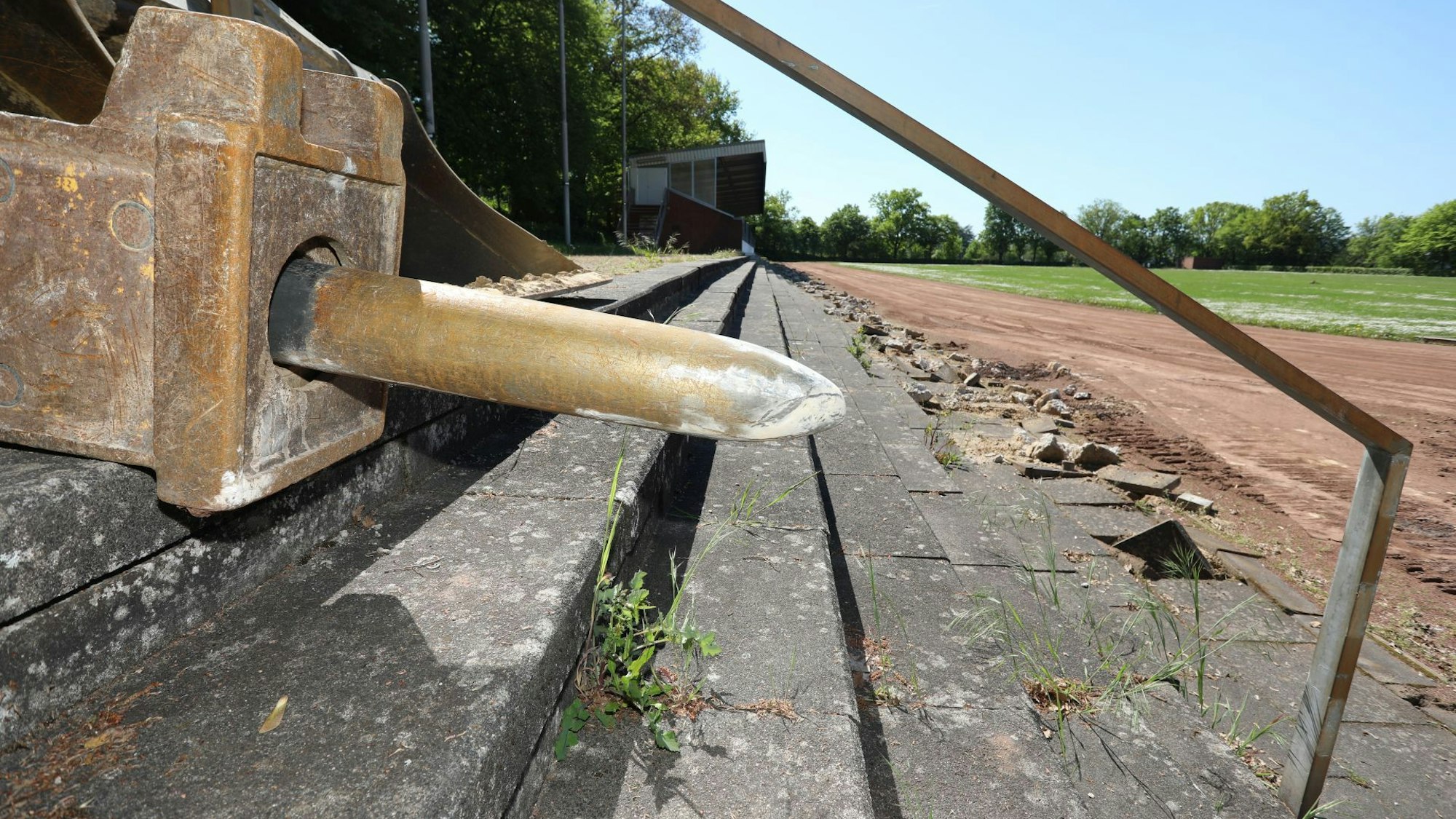 Der überdimensionale Meißel eines Baggers liegt auf Sitzstufen aus Beton, die stark beschädigt sind.