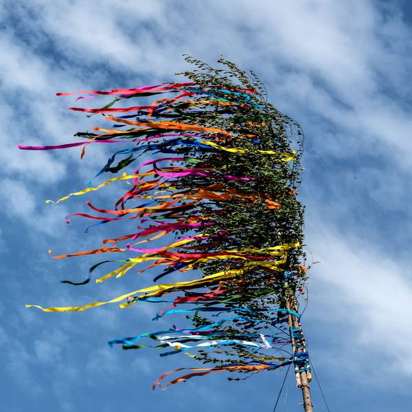 Bunte Bänder eines Maibaumes flattern vor dem blauen Himmel.