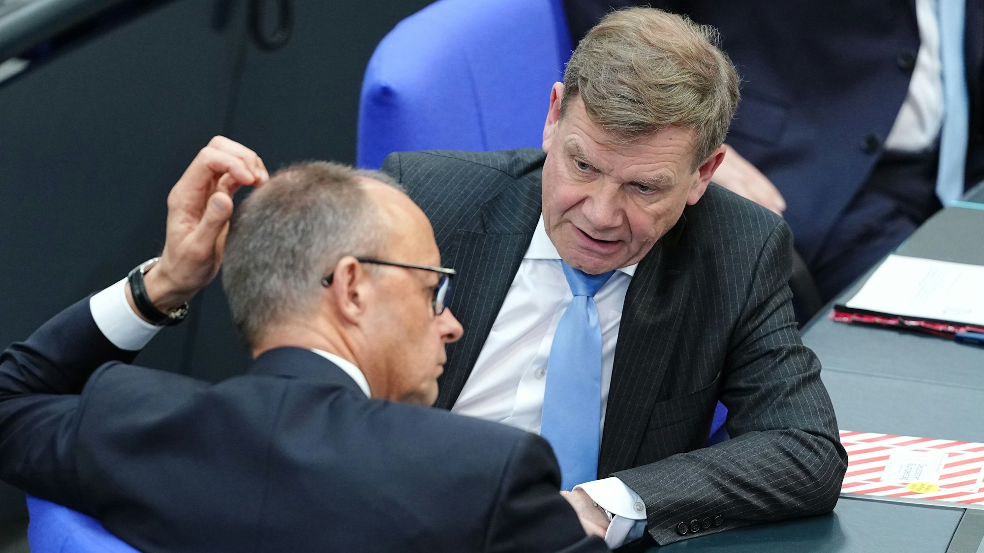 Zwei Politiker sitzen im Bundestag und sprechen miteinander.