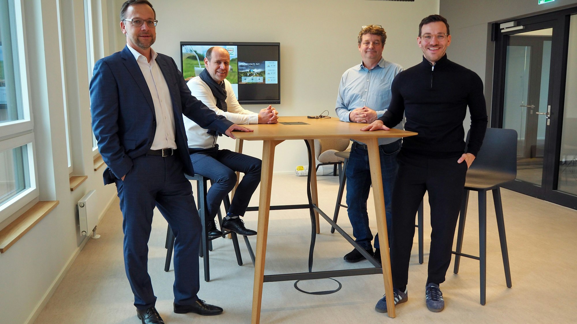 Vier Männer stehen an einem Hochtisch in einem Besprechenungsraum.