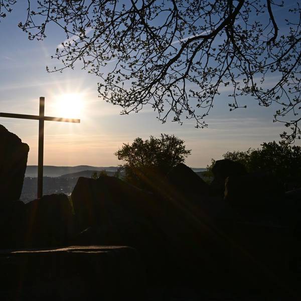 Die Sonne geht vor einem Kreuz am Birkenkopf auf. Der Birkenkopf ist ein künstlicher Hügel, aufgeschüttet aus Ruinen aus dem 2. Weltkrieg.