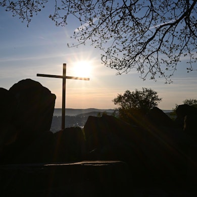 Die Sonne geht vor einem Kreuz am Birkenkopf auf. Der Birkenkopf ist ein künstlicher Hügel, aufgeschüttet aus Ruinen aus dem 2. Weltkrieg.