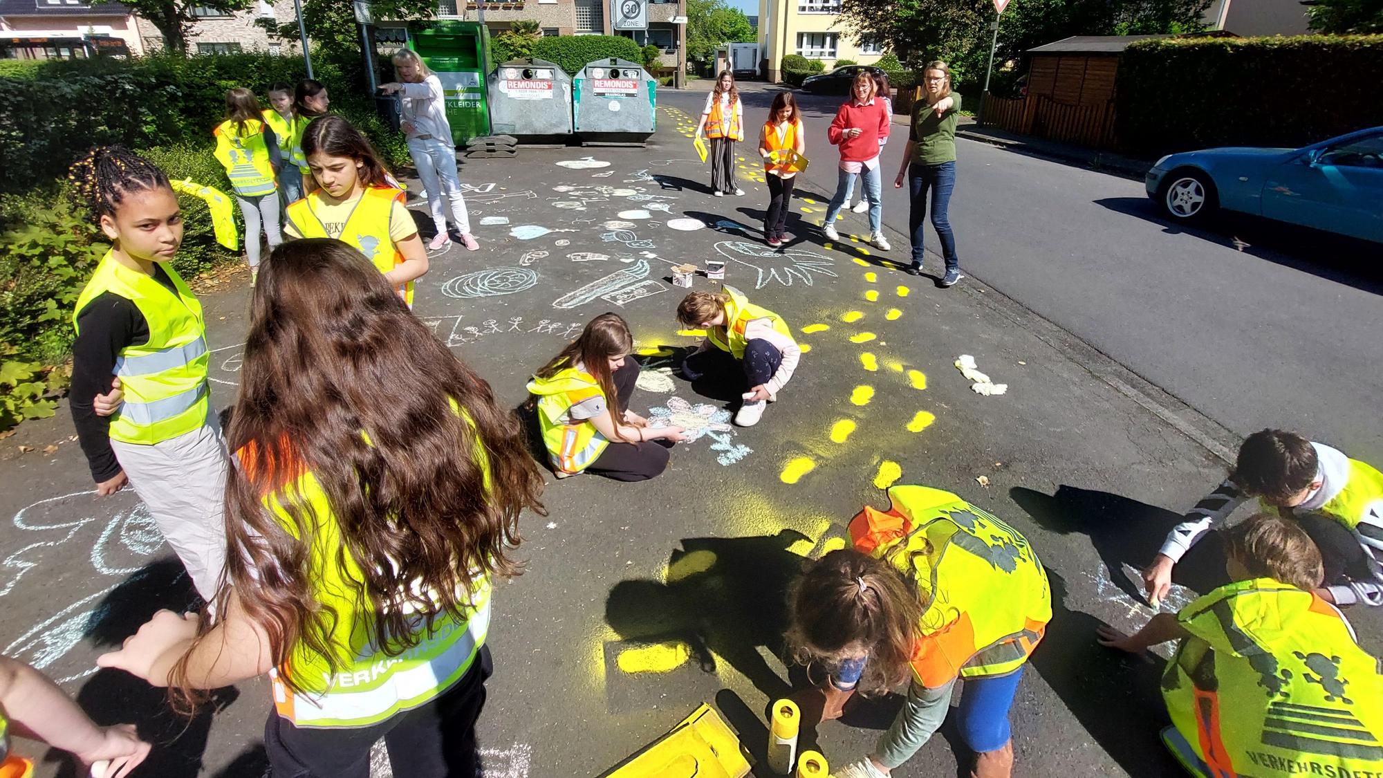 Kinder in Warnwesten bemalen einen Gehweg.