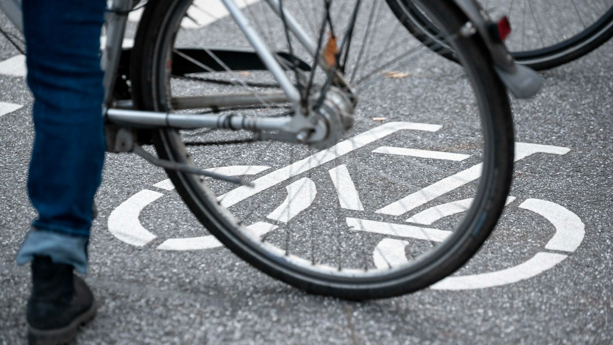 Ein Fahrrad-Symbol ist auf der Fahrbahn einer Straße hinter einem Fahrrad zu sehen.