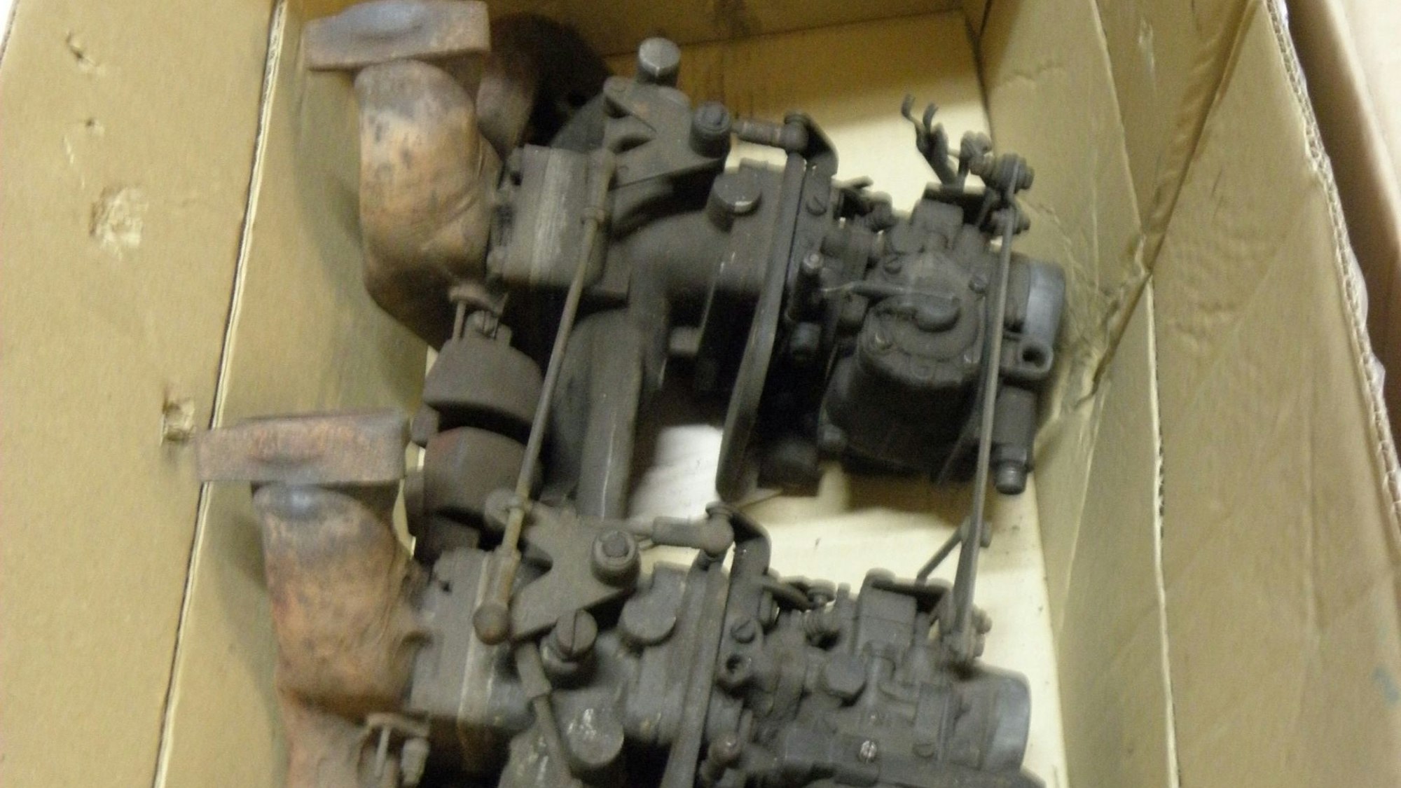 In einem Pappkarton liegen schmutzige und ölverschmierte Teile eines Automotors.