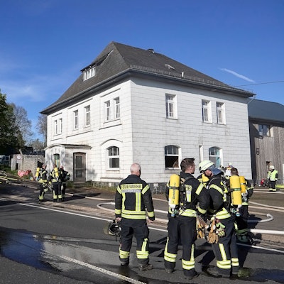 Feuerwehrleute stehen vor einem Haus in Hellenthal-Kehr, in dem es gebrannt hat.