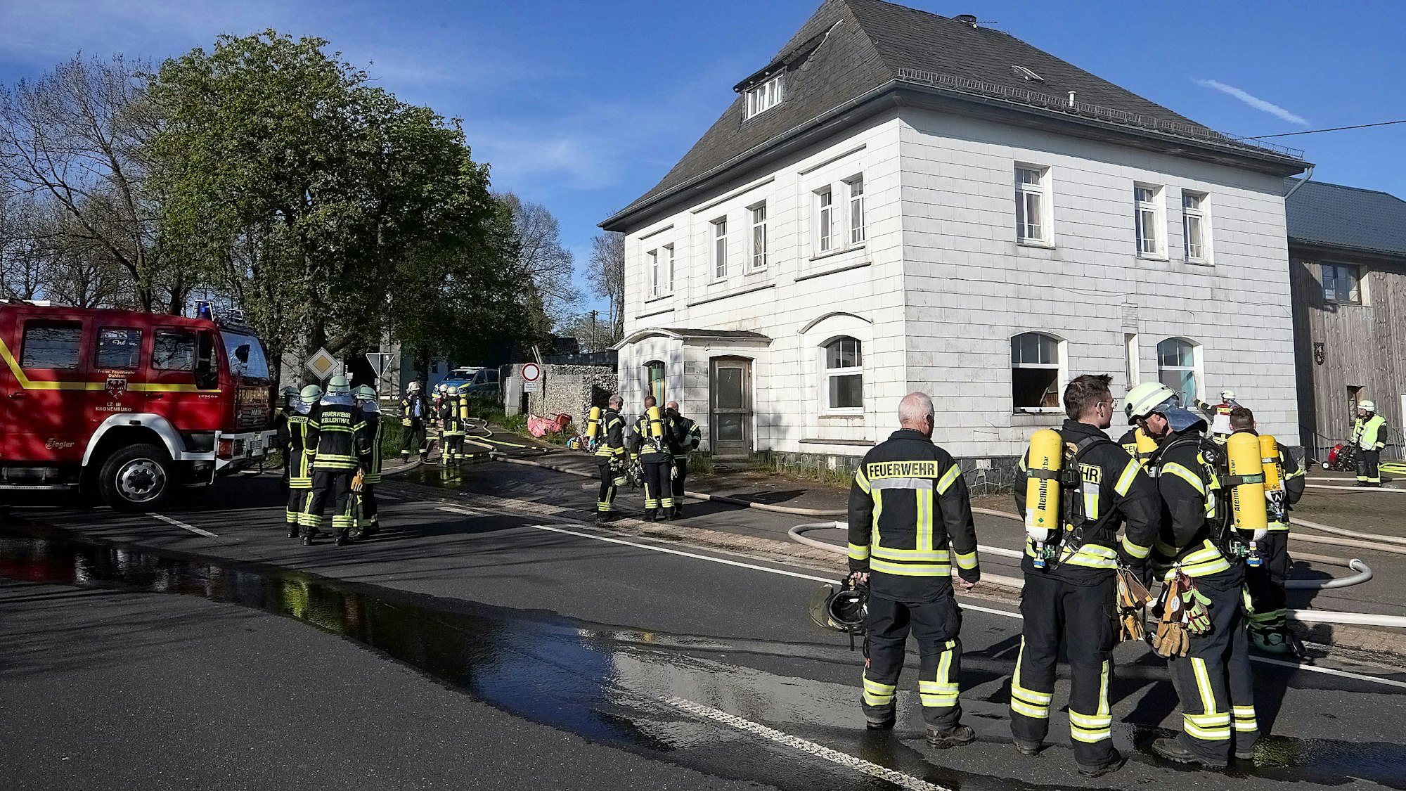 Feuerwehrleute stehen vor einem Haus in Hellenthal-Kehr, in dem es gebrannt hat.