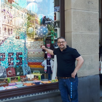 Inhaber Marc Düssel vor seinem reich dekorierten Schaufenster mit der Nippes-Hommage aus Pailletten.