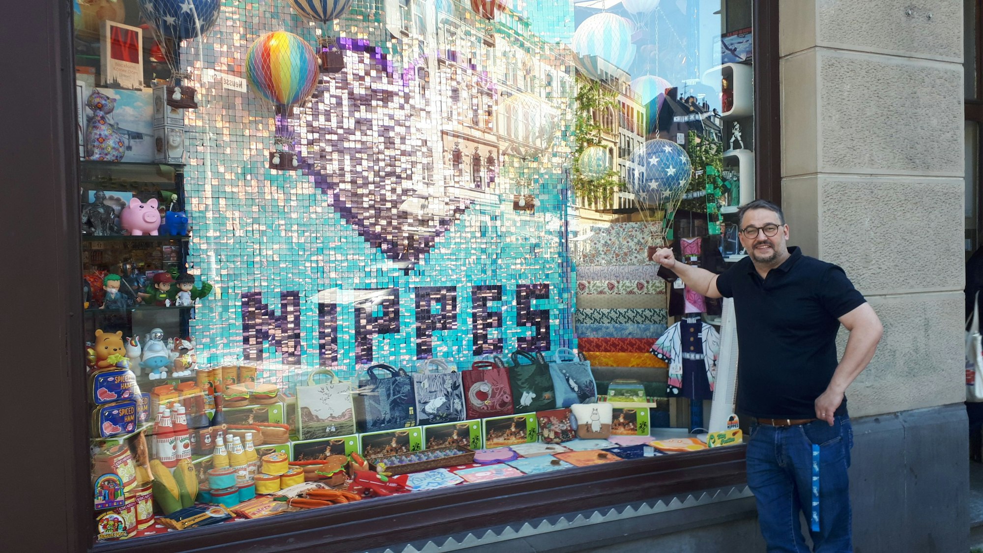 Inhaber Marc Düssel vor seinem reich dekorierten Schaufenster mit der Nippes-Hommage aus Pailletten.
