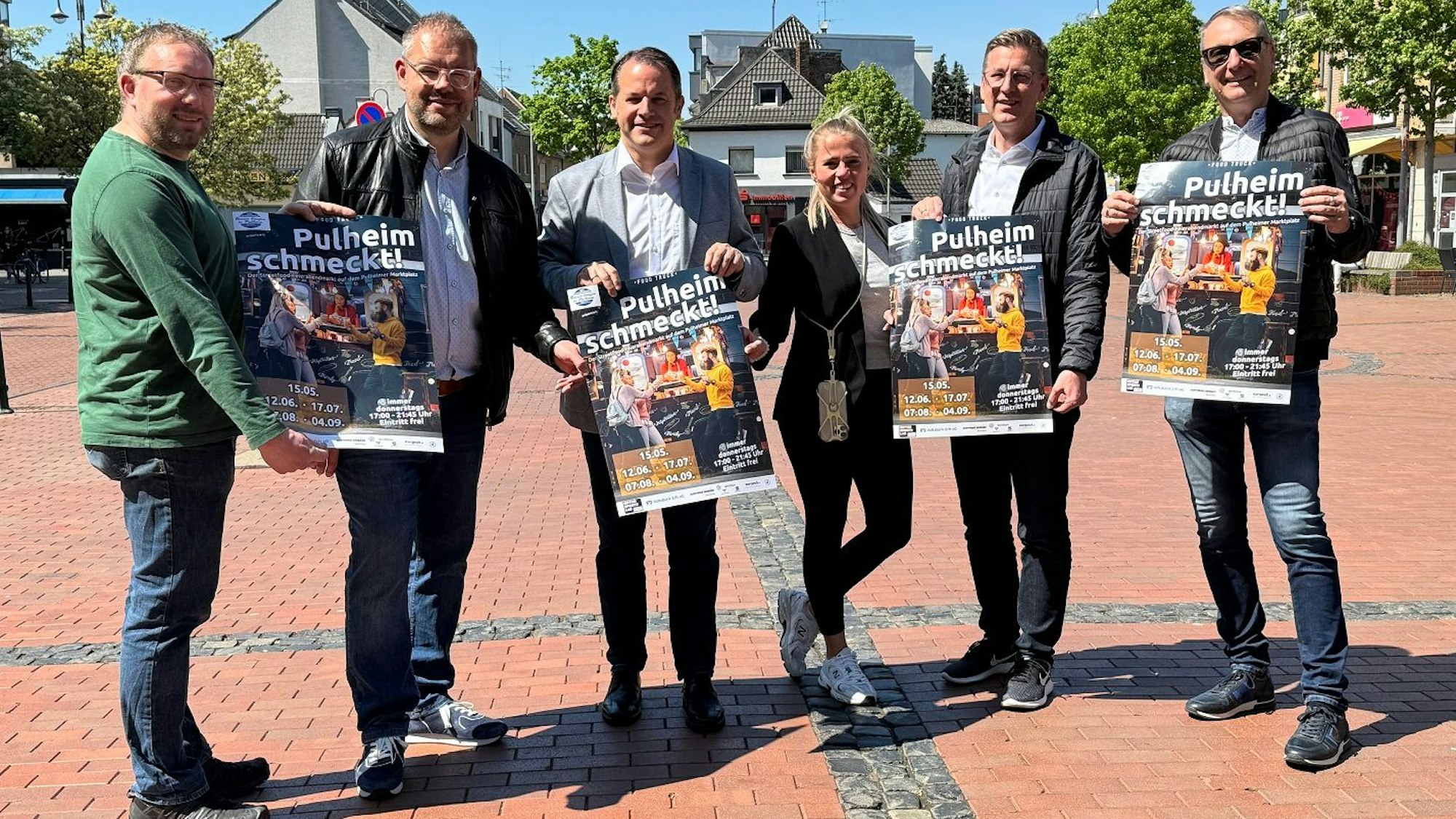 Eine Frau und fünf Männer halten Plakate mit der Aufschrift „Pulheim schmeckt “in die Kamera.