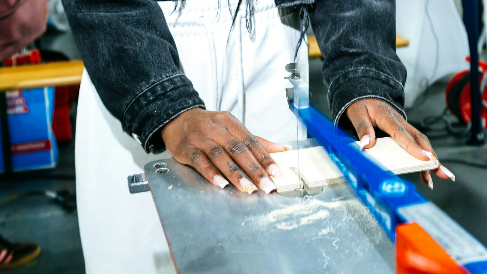Man sieht zwei Hände eines jungen Mädchens, die ein dünnes Stück Holz unter eine Dekupiersäge hält.