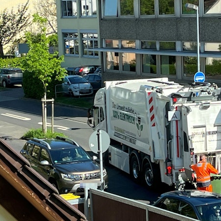 Ein elektrischer Müllwagen in Hennef. Ein Arbeiter rollt eine grüne Papiertonne zum Fahrzeug.