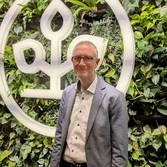 Helmut Schneider steht vor einer begrünten Wand mit einem AOK-Emblem.