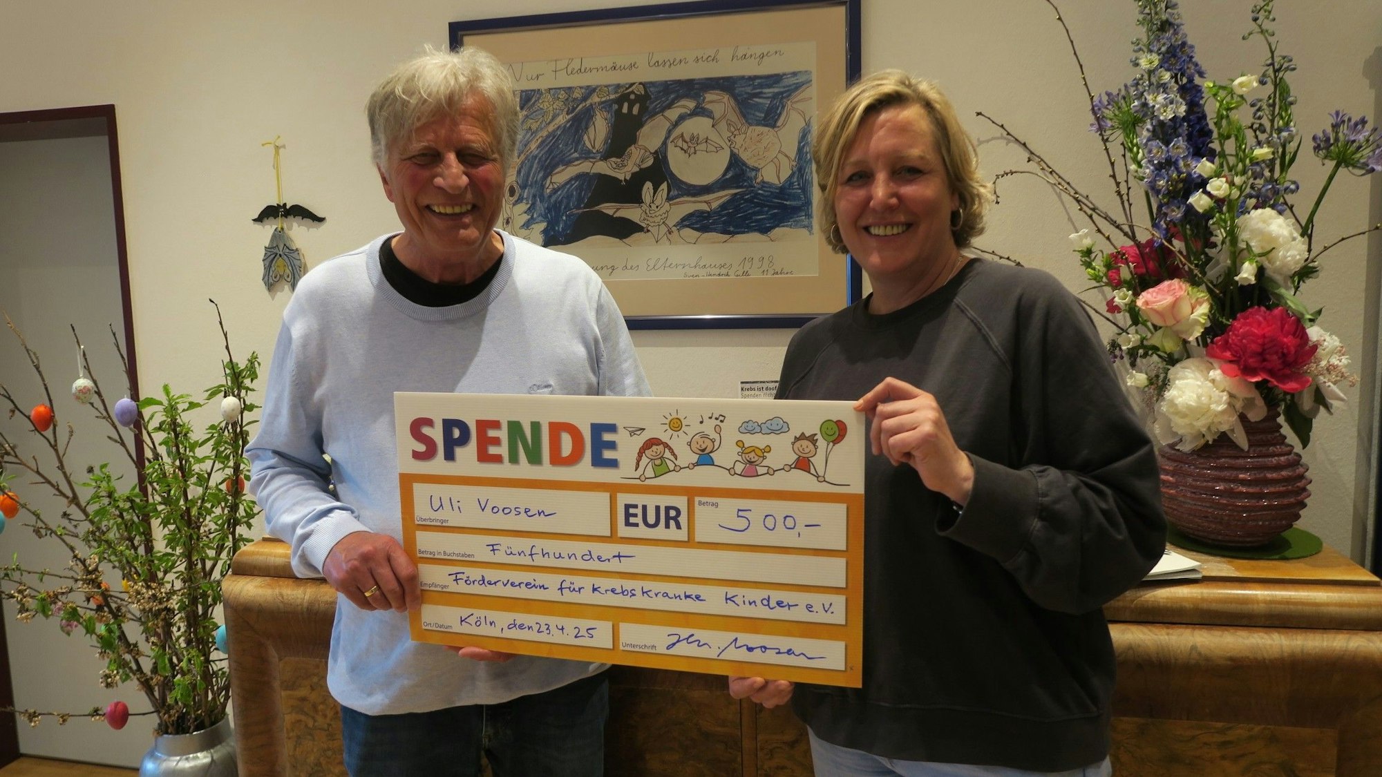 Ein Mann und eine Frau halten gemeinsam einen gemalten überdimensionierten Scheck über 500 Euro hoch.