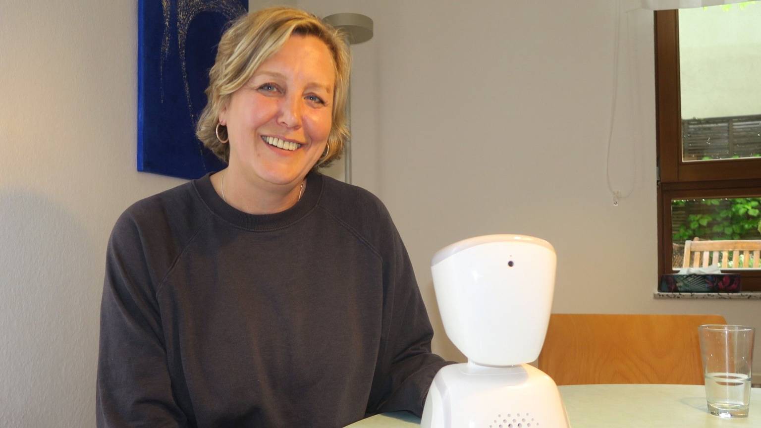 Eine blonde Frau sitzt an einem Tisch, auf dem ein elektronischer Apparat steht.