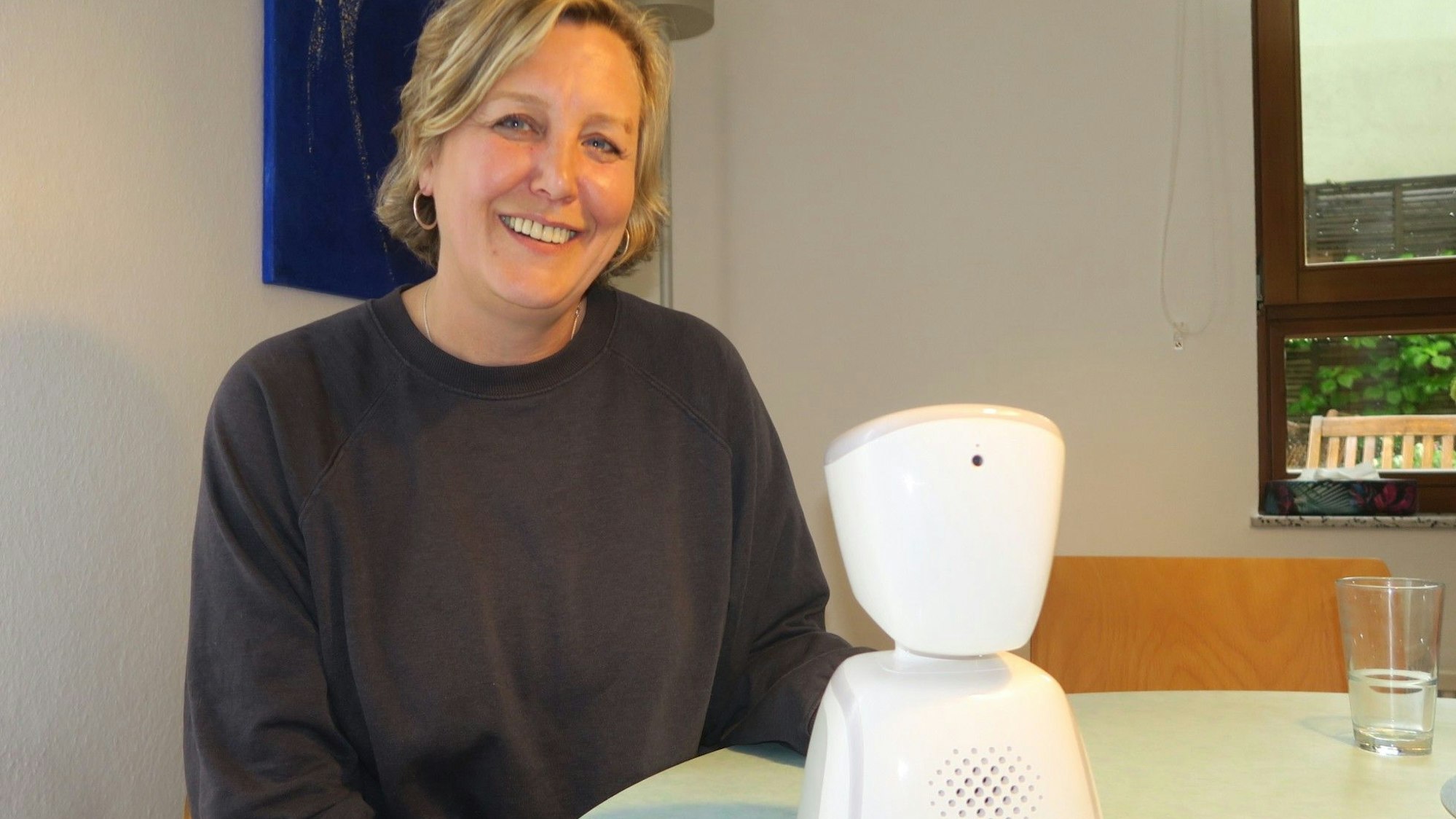 Eine blonde Frau sitzt an einem Tisch, auf dem ein elektronischer Apparat steht.