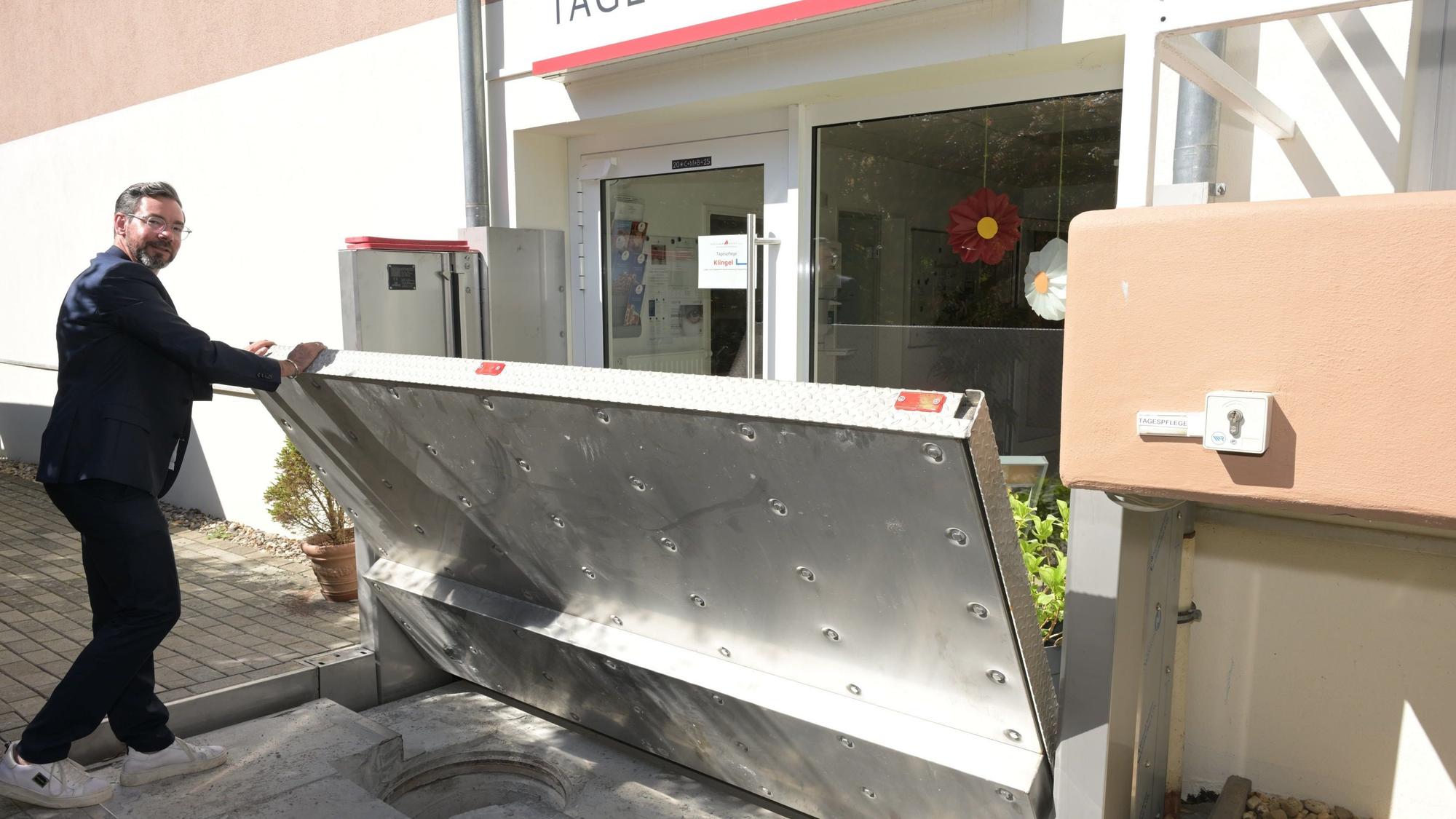 Vor der Tagespflege des Wöllner-Stifts in Rösrath-Hoffnungsthal zeigt Geschäftsführer Michael Heine, wie eine Edelstahl-Wand im Fall von Hochwasser automatisch hochgefahren wird.