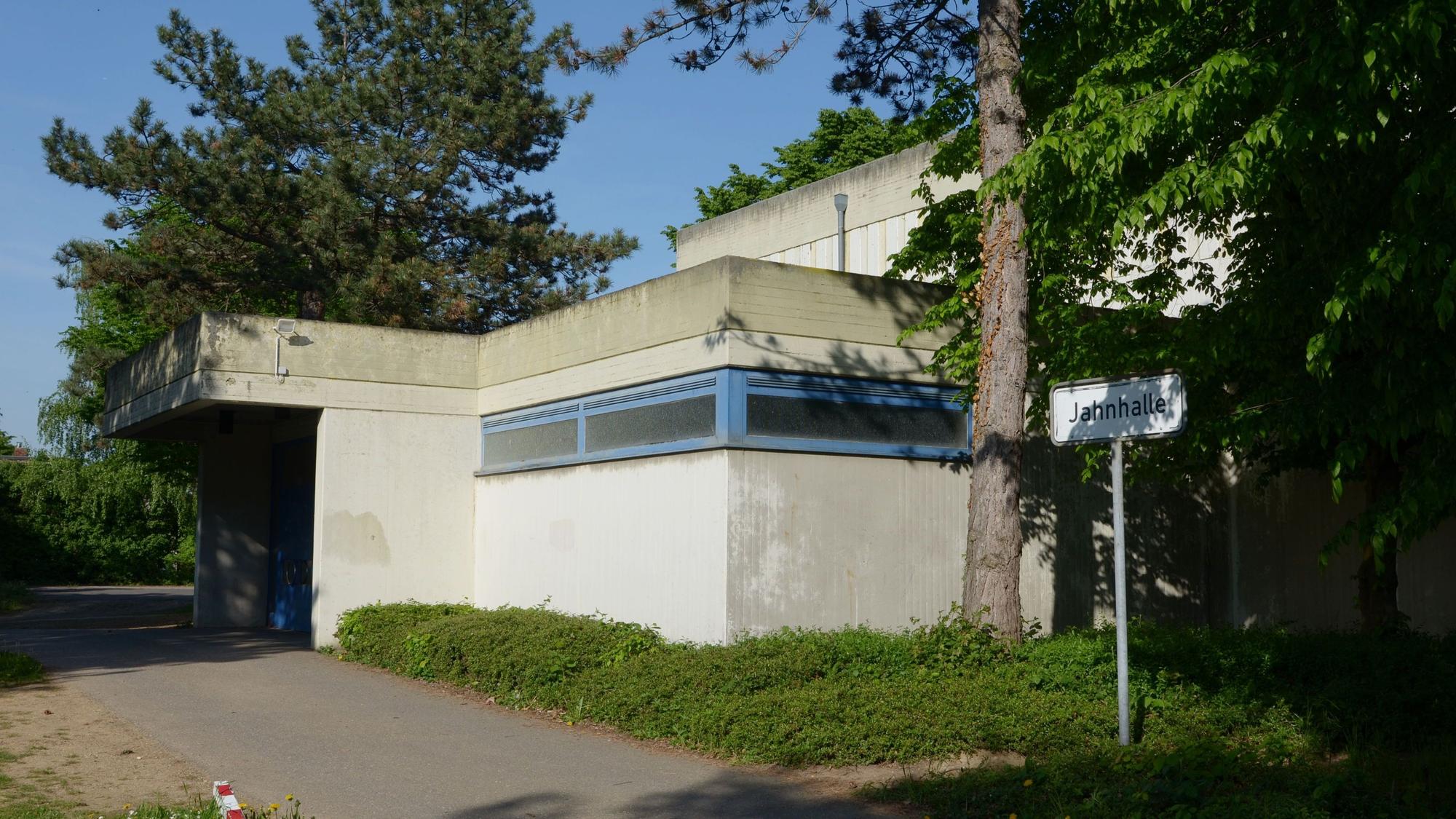 Das Bild zeigt den Eingang der Halle, die von Bäumen umgeben ist.