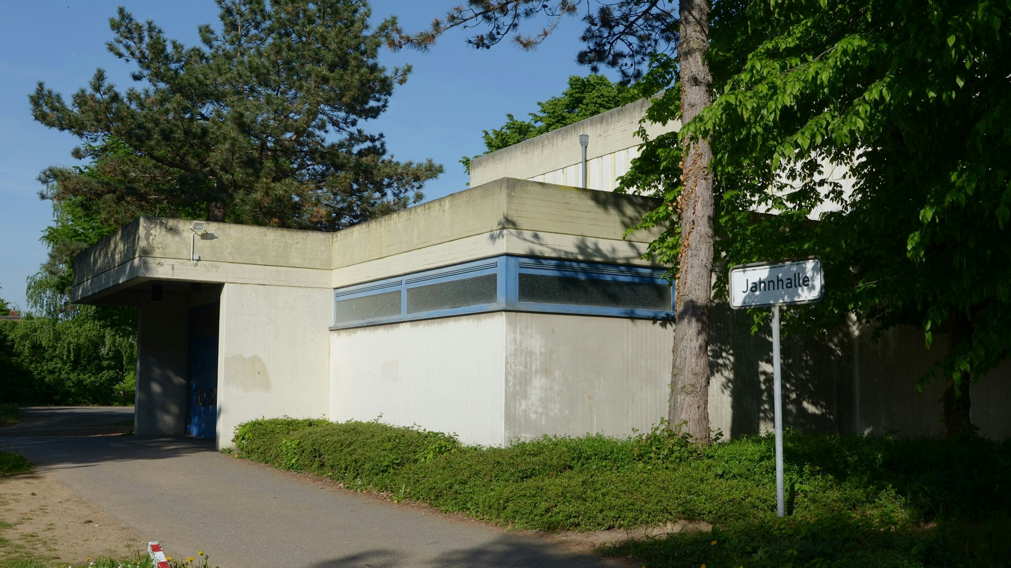 Das Bild zeigt den Eingang der Halle, die von Bäumen umgeben ist.