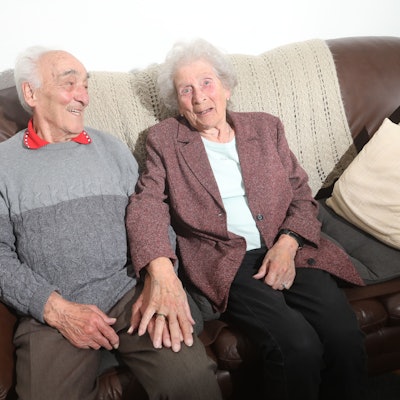 Ein älteres Ehepaar sitzt auf einer braunen Couch.