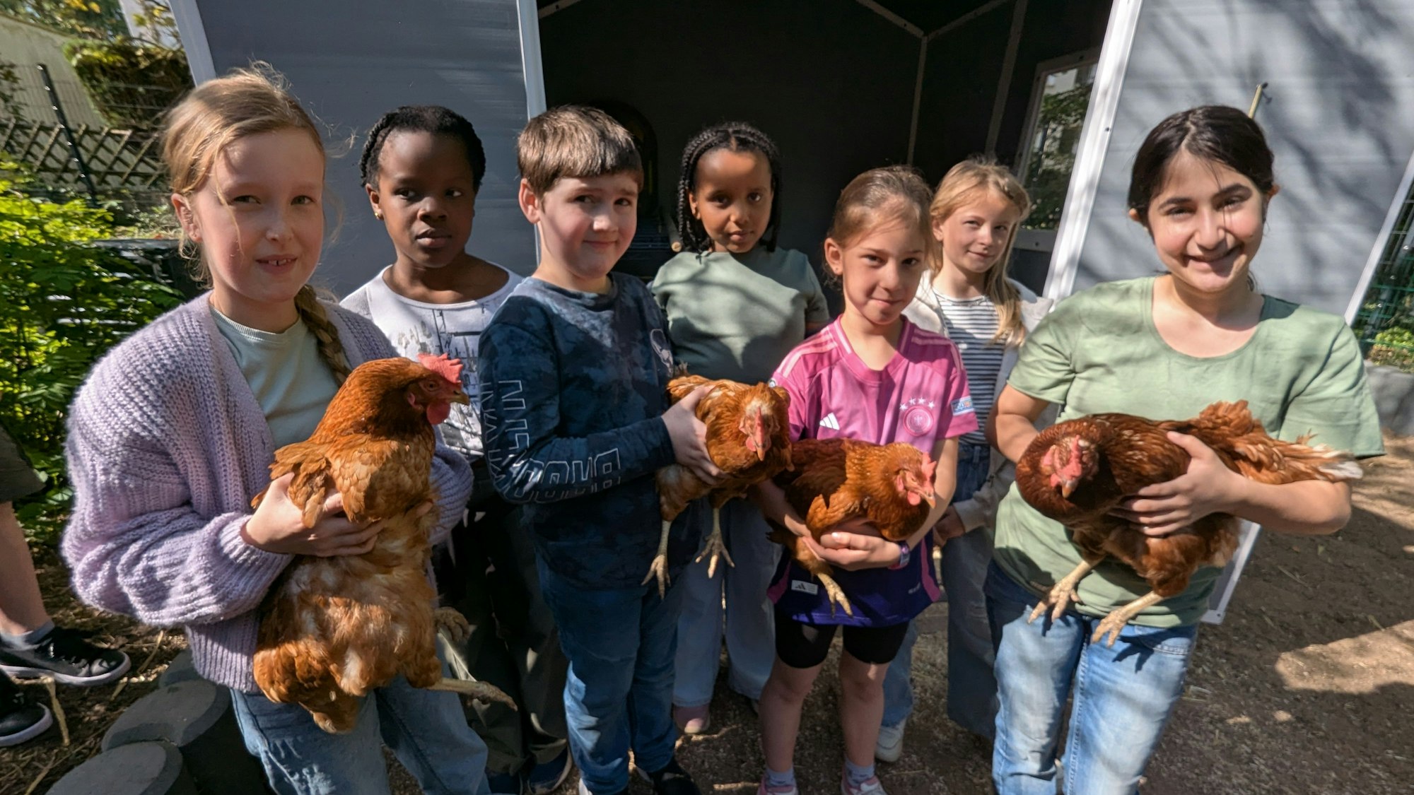Das Foto zeigt Schulkinder vor dem Hühnerstall, die die Hennen in den Armen halten.