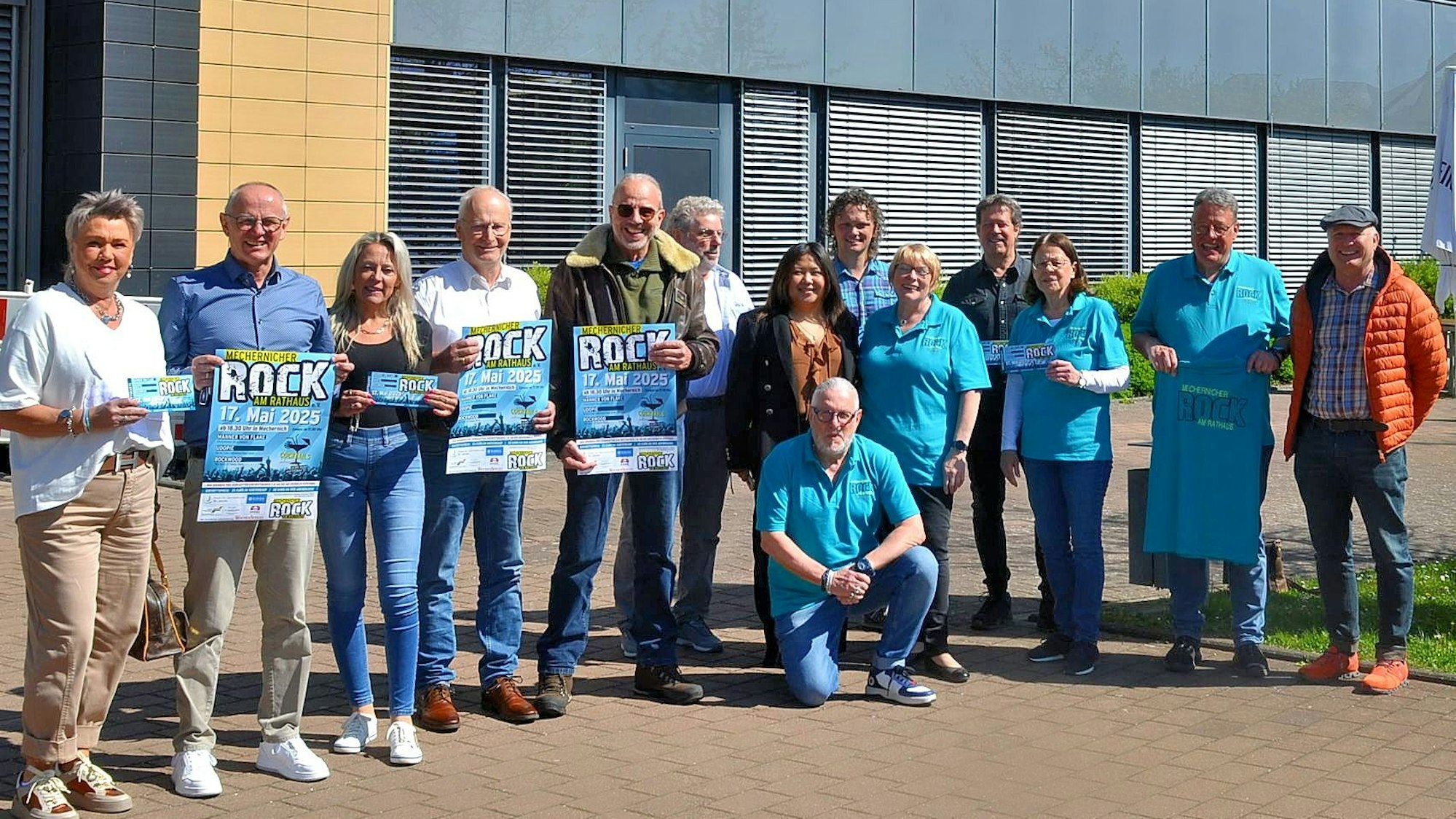 Eine Gruppe Menschen steht, zum Teil in türkisblauen Poloshirts gekleidet, vor dem Mechernicher Rathaus.