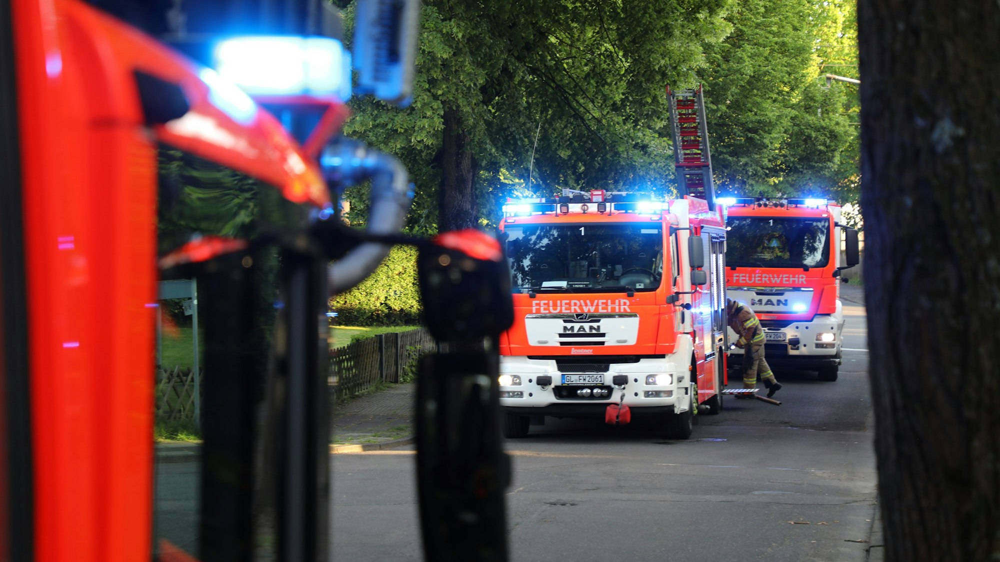 Feuerwehrautos stehen in einer Wohnstraße mit Alleebäumen.