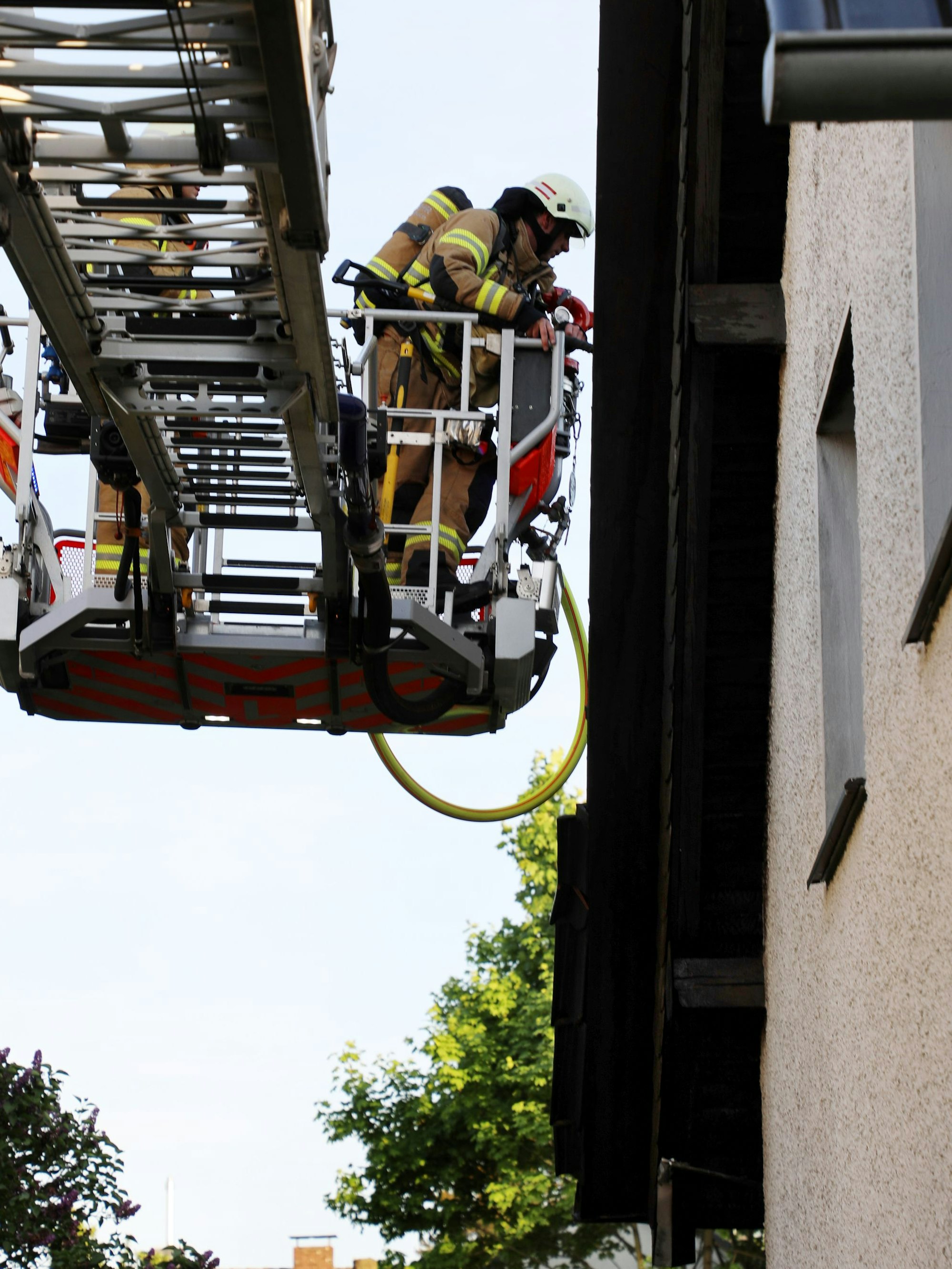 Feuerwehrleute decken aus einem Korb einer Drehleiter Dachpfannen ab.