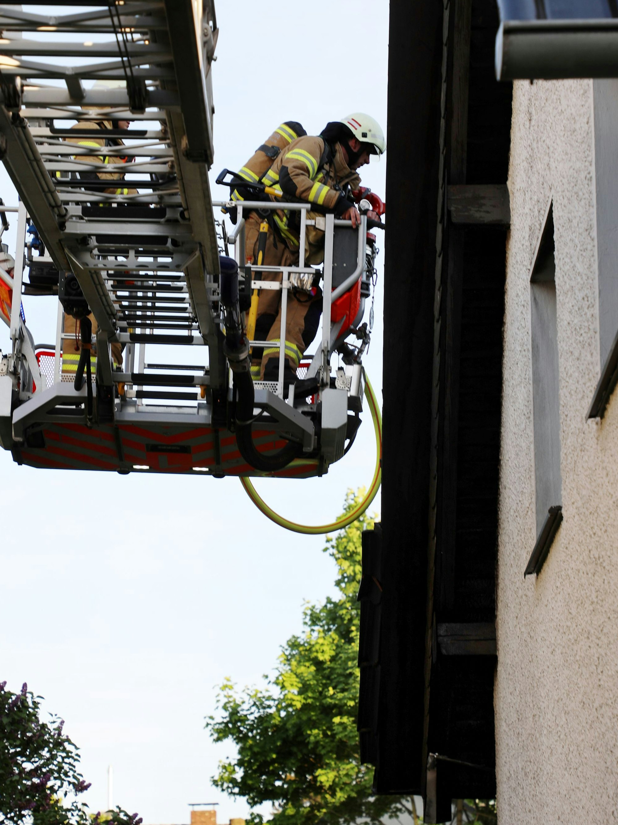Feuerwehrleute decken aus einem Korb einer Drehleiter Dachpfannen ab.