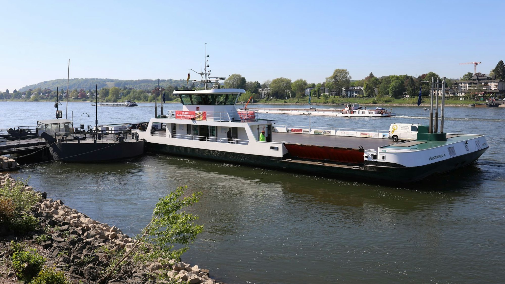 Die Rheinfähre am Anleger in Königswinter, im Hintergrund führt ein Frachtschiff vorbei.